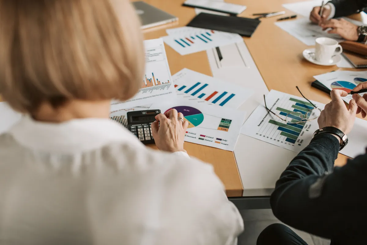 Advisors and a client analyzing portfolio charts and performance data with a calculator during an investment management meeting