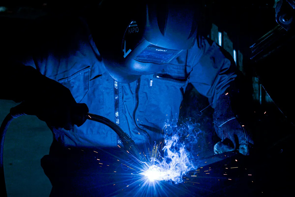 A welder fusing steel with a focused electric arc, sending up a burst of bright blue sparks